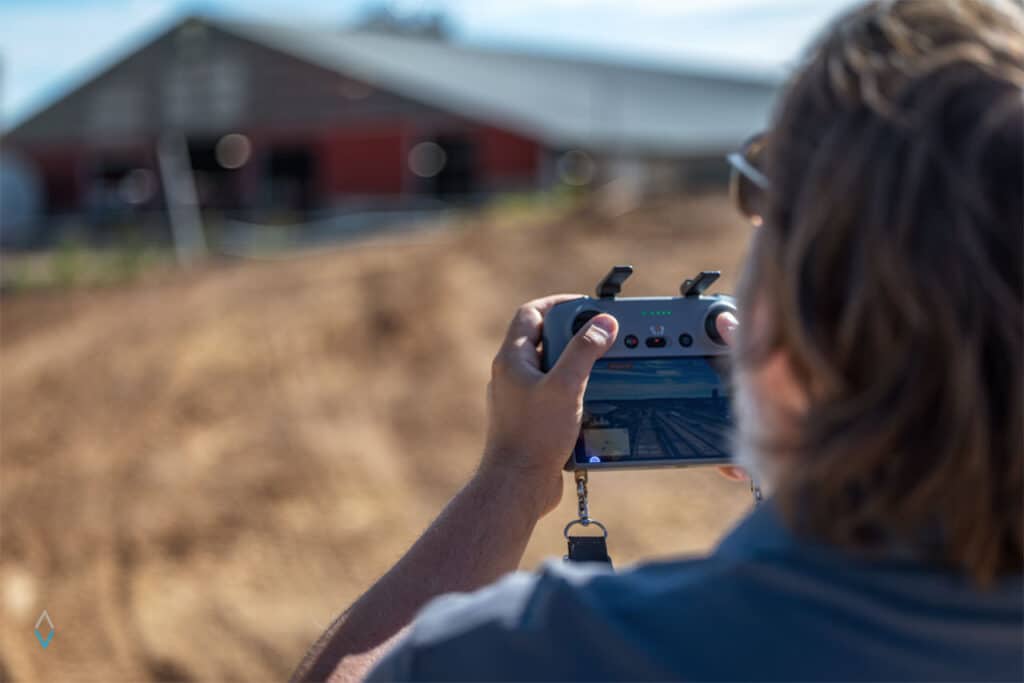Tyler Kimpel, FAA Part 107 certified drone pilot, flying a drane with the control interface near a modern dairy barn in Wisconsin.